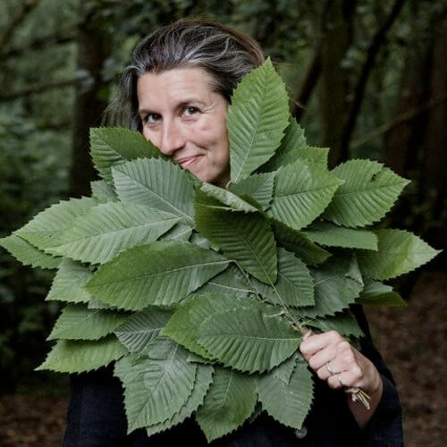 Smiling woman hiding her upper body behind a fan of leaves