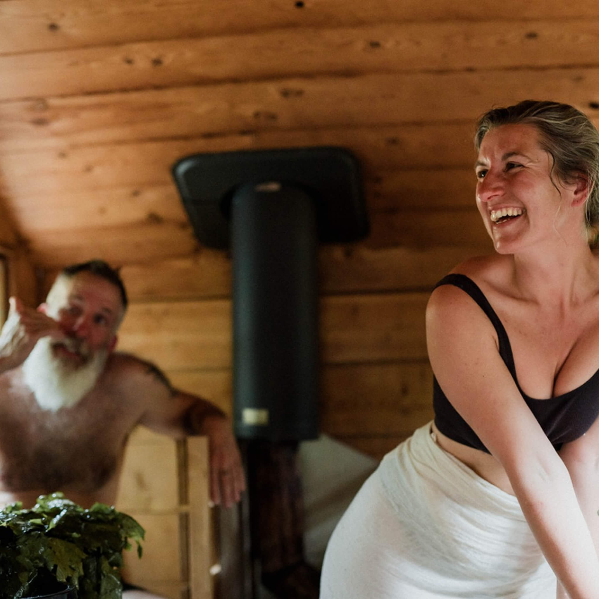 A happy woman and a man with long white beard inside a wooden sauna