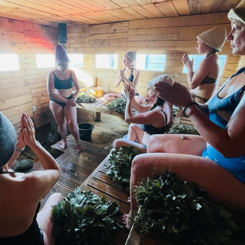 a group of people inside a sauna participating in a Leaf Whisking ritual