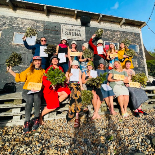 A group of cheering students holding up a certificate outside a wooden sauna building