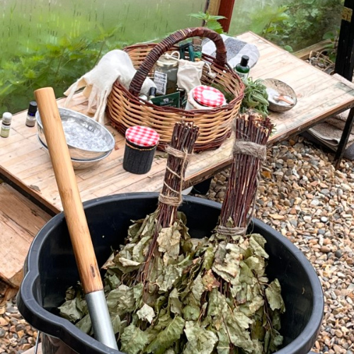 A bucket with bunches of twigs with leaves and a table with a basket and items for sauna practice